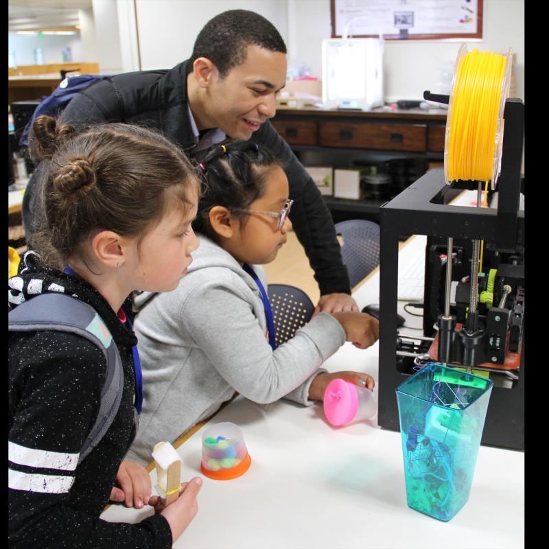 ECS Alumni and University Elementary Teacher Ryan Kurada showing students the 3D printer Teacher showing 3D printer to students